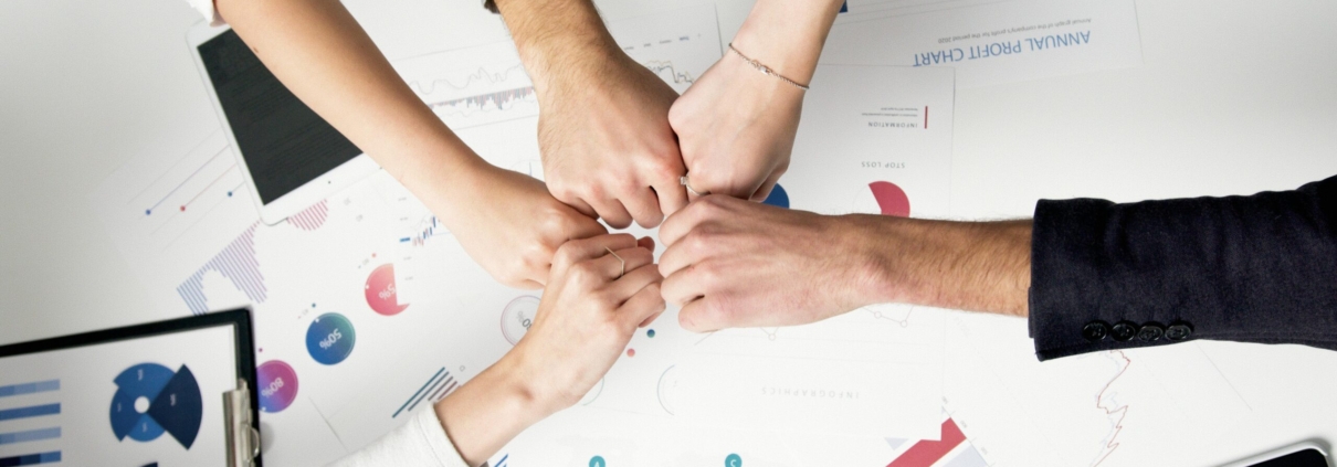Free Colleagues celebrate success with a fist bump over financial charts depicting teamwork and unity. Stock Photo