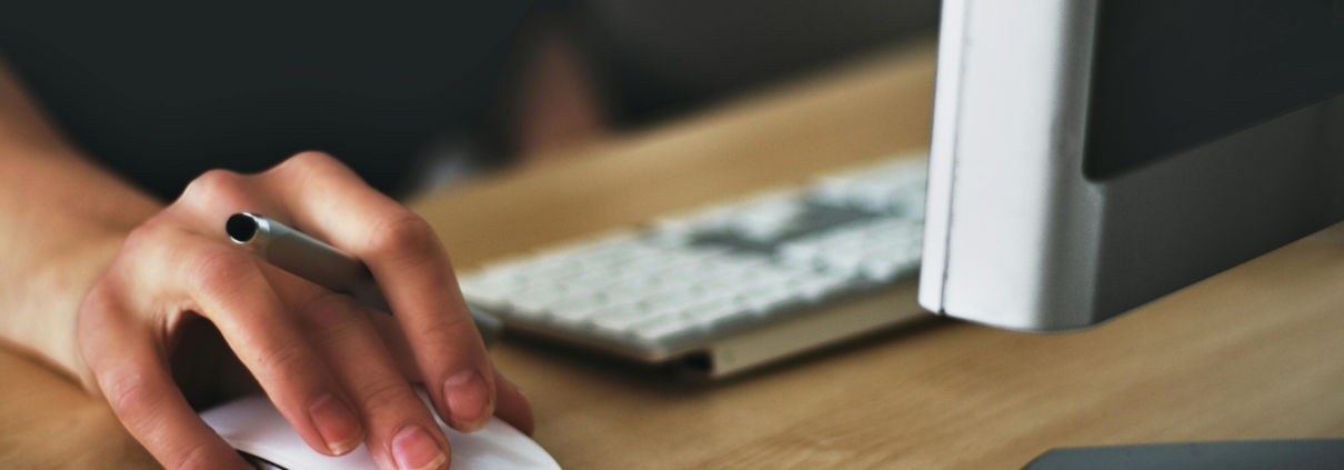 Free A hand using a wireless mouse at a modern desk setup with a computer and keyboard. Stock Photo